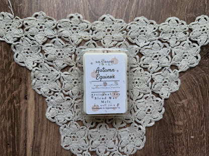 An Autumn Equinox wax melt by Lil Daisy Soaps rests on lace atop a wooden surface.