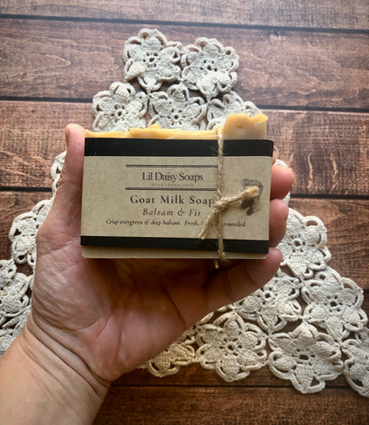 Hand holding Lil Daisy Soaps Balsam & Fir Goat Milk Soap with lace doily and wood background.