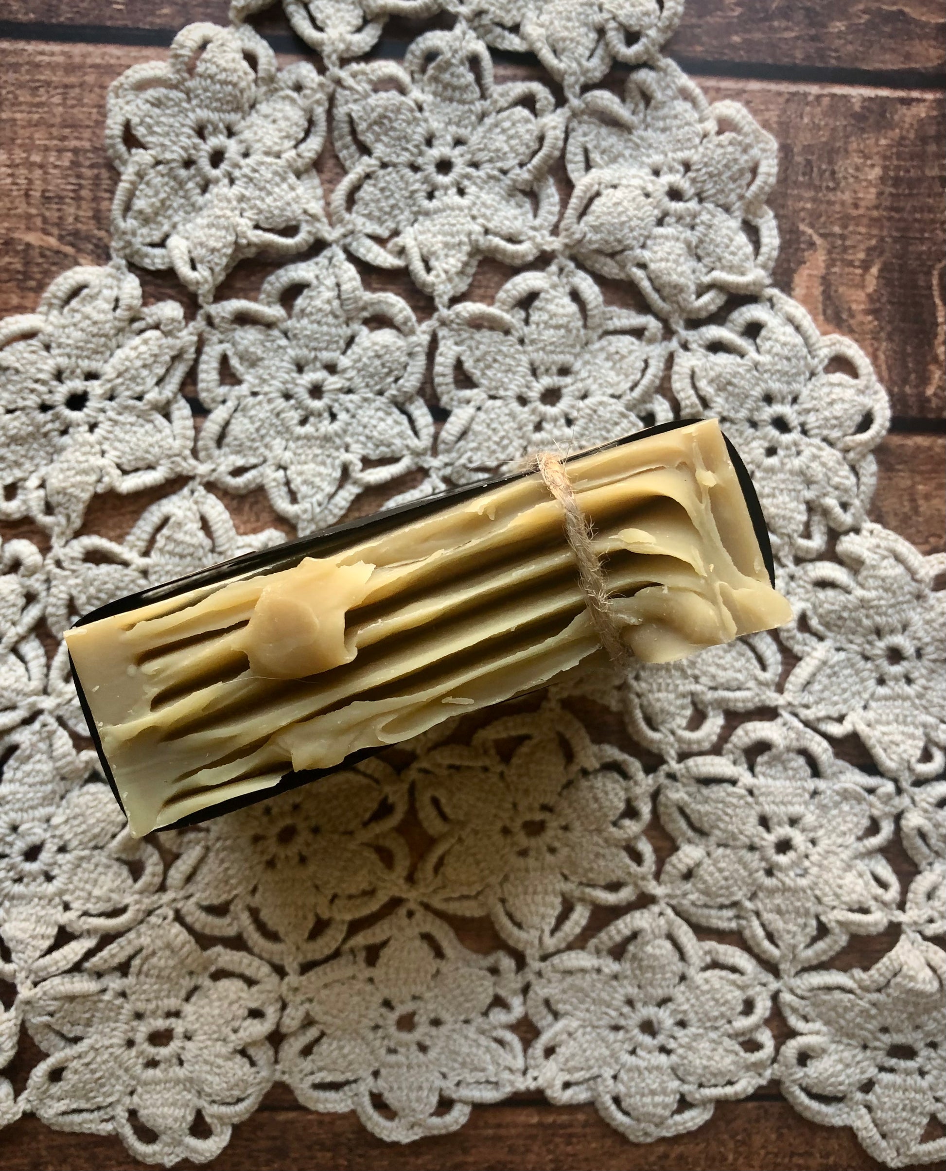 Lil Daisy Soaps Balsam & Fir Goat Milk Soap bar sits on a crocheted doily atop a wooden surface.