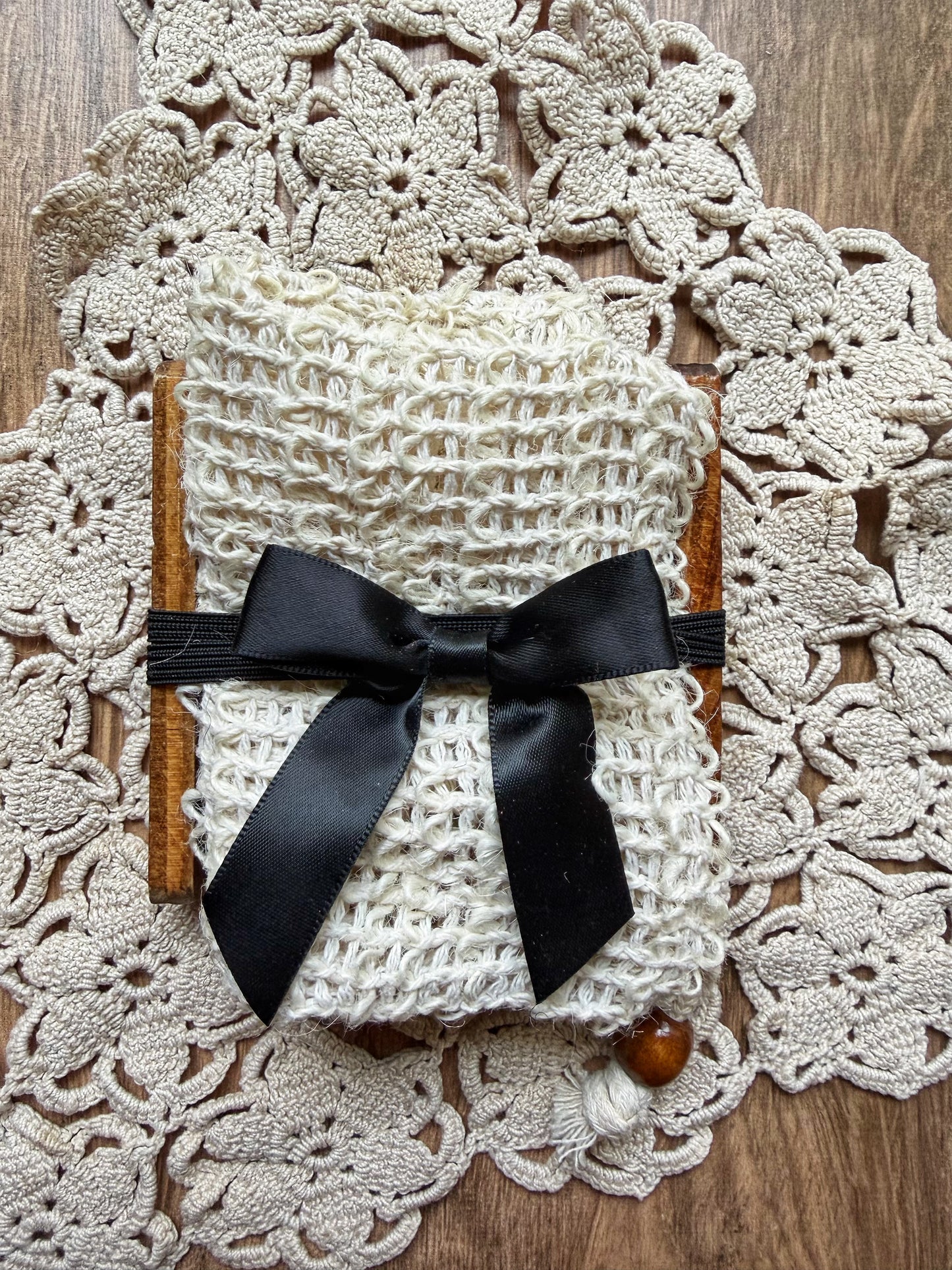 A Lil Daisy Soaps Bamboo Soap Ladder & Natural Fiber Soap Saver, tied with black ribbon on a lacy doily.