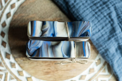 Two Lil Daisy Soaps Amberwood Goat Milk Soap Bars, handcrafted and tied with twine on a wooden surface.