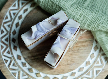 Two Lil Daisy Soaps Berries & Cream Goat Milk Soap bars with purple swirls, gentle on skin, on a wooden tray.