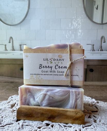 Two Lil Daisy Soaps Berry Creme Goat Milk bars with rustic labels rest on a crochet mat in a bathroom.