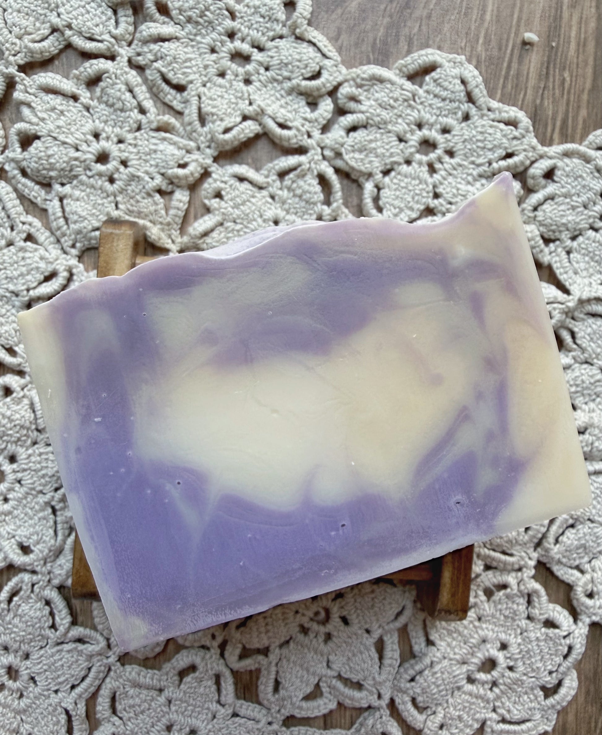 A Berry Creme Natural Goat Milk Soap Bar by Lil Daisy Soaps sits on a wood dish on a lace doily.