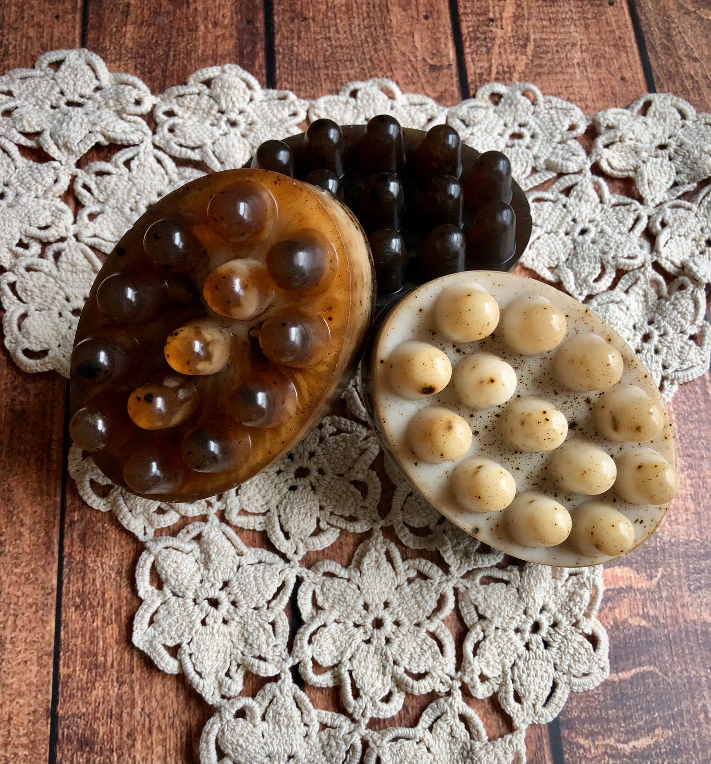 Three Lil Daisy Soaps Coffee & Cream Massage Bars with nubs rest on a crocheted doily atop wood.