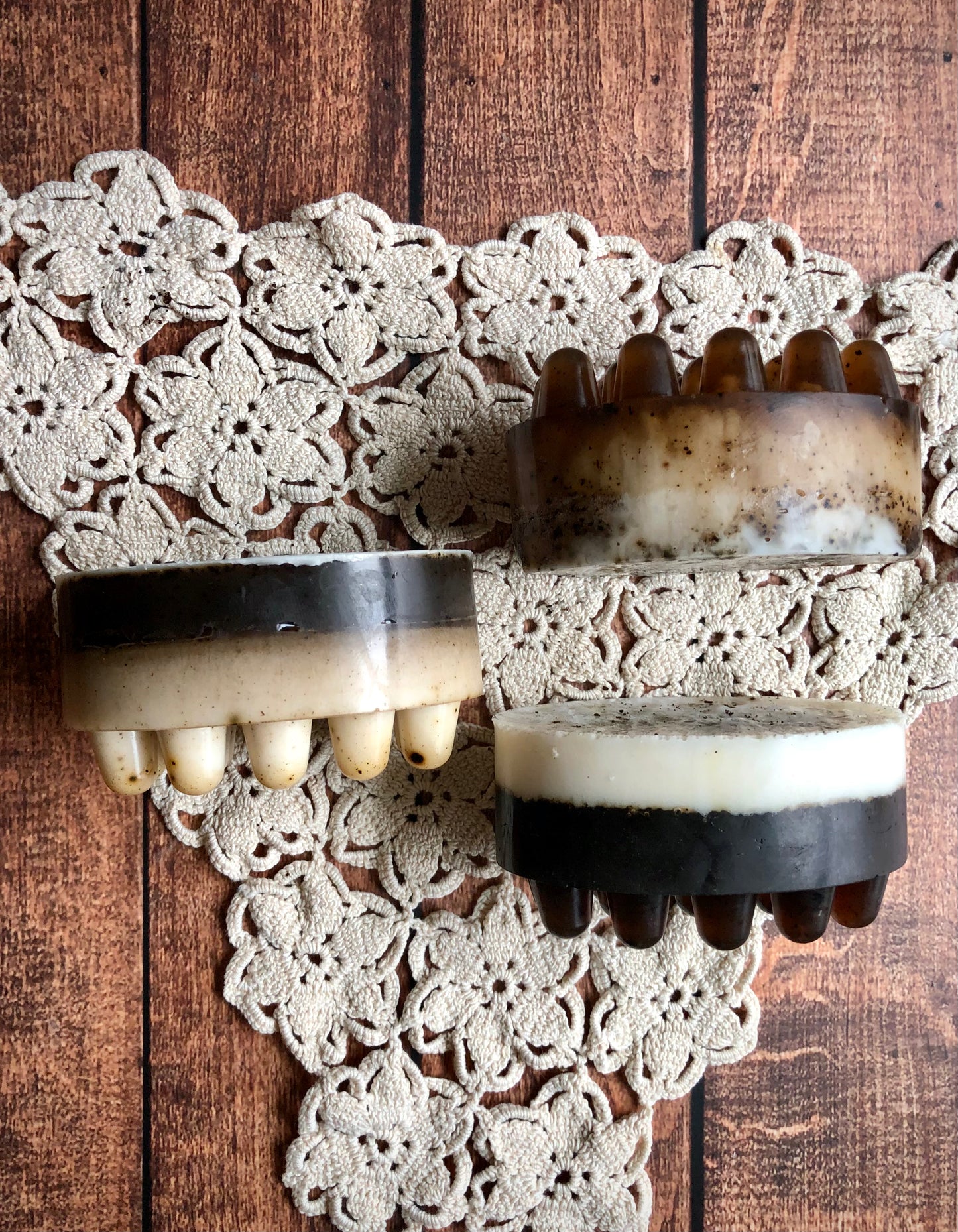 The Coffee & Cream Massage Soap Bar by Lil Daisy Soaps rests on a crocheted doily atop wood.
