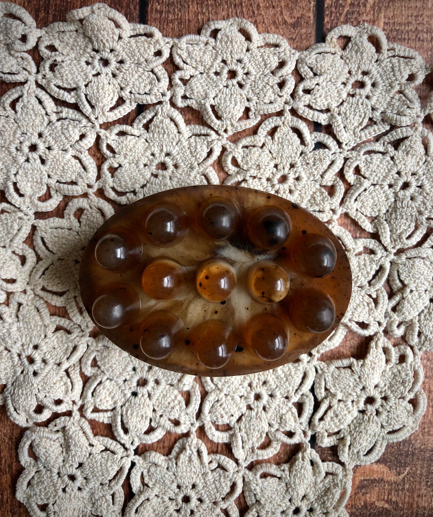 Lil Daisy Soaps Coffee & Cream Massage Soap Bar, oval and brown with bumps, on cream lace over wood.