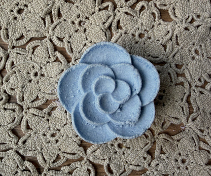 A blue Essential Oil Shower Steamer by Lil Daisy Soaps sits on a beige crocheted floral-patterned surface.