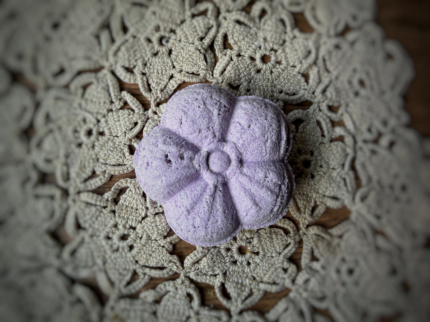 A purple Essential Oil Shower Steamer by Lil Daisy Soaps sits on a lace doily, perfect for aromatherapy.