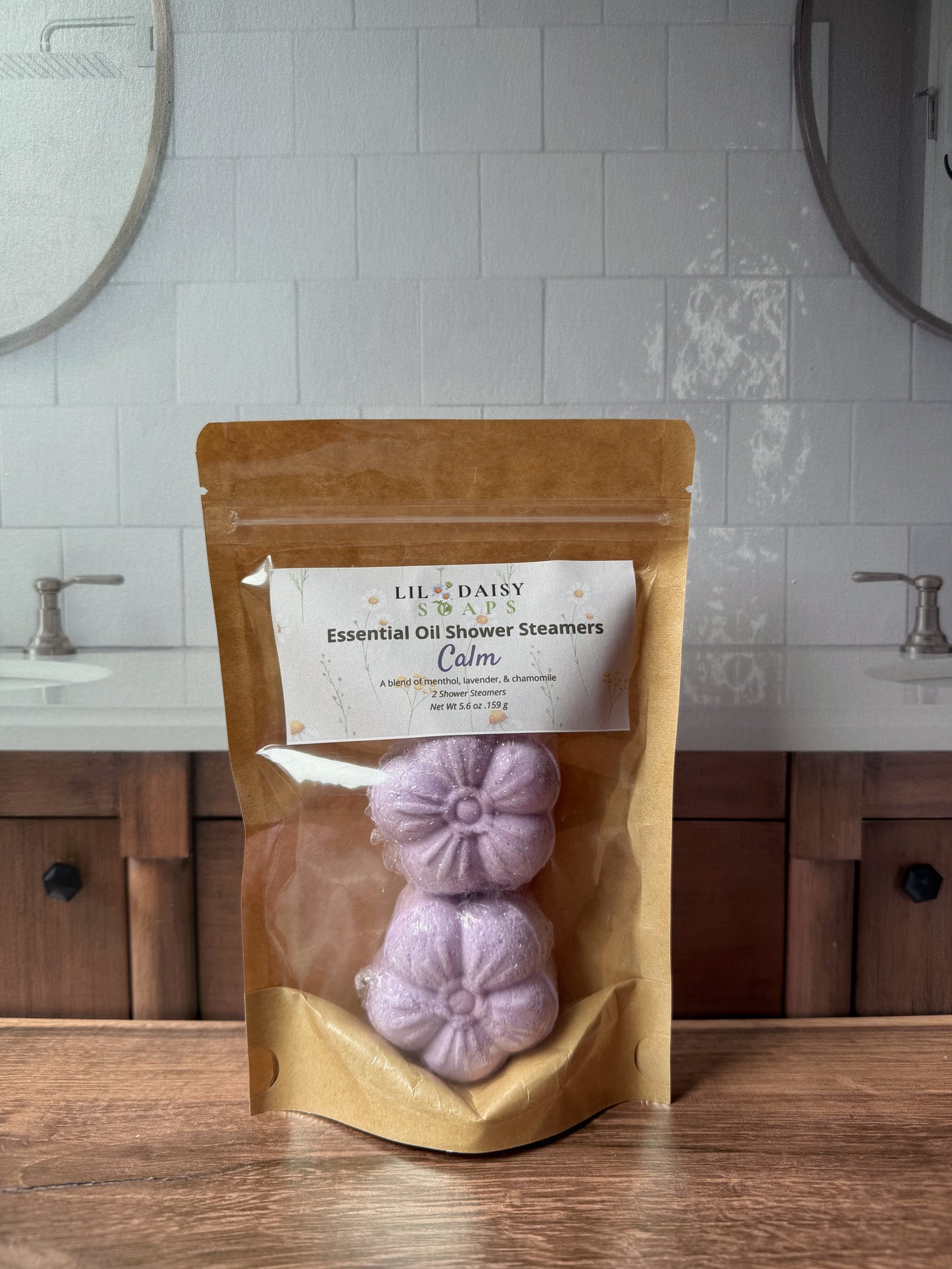 Lil Daisy Soaps Essential Oil Shower Steamers in Calm rest on a wooden bathroom counter in a brown bag.