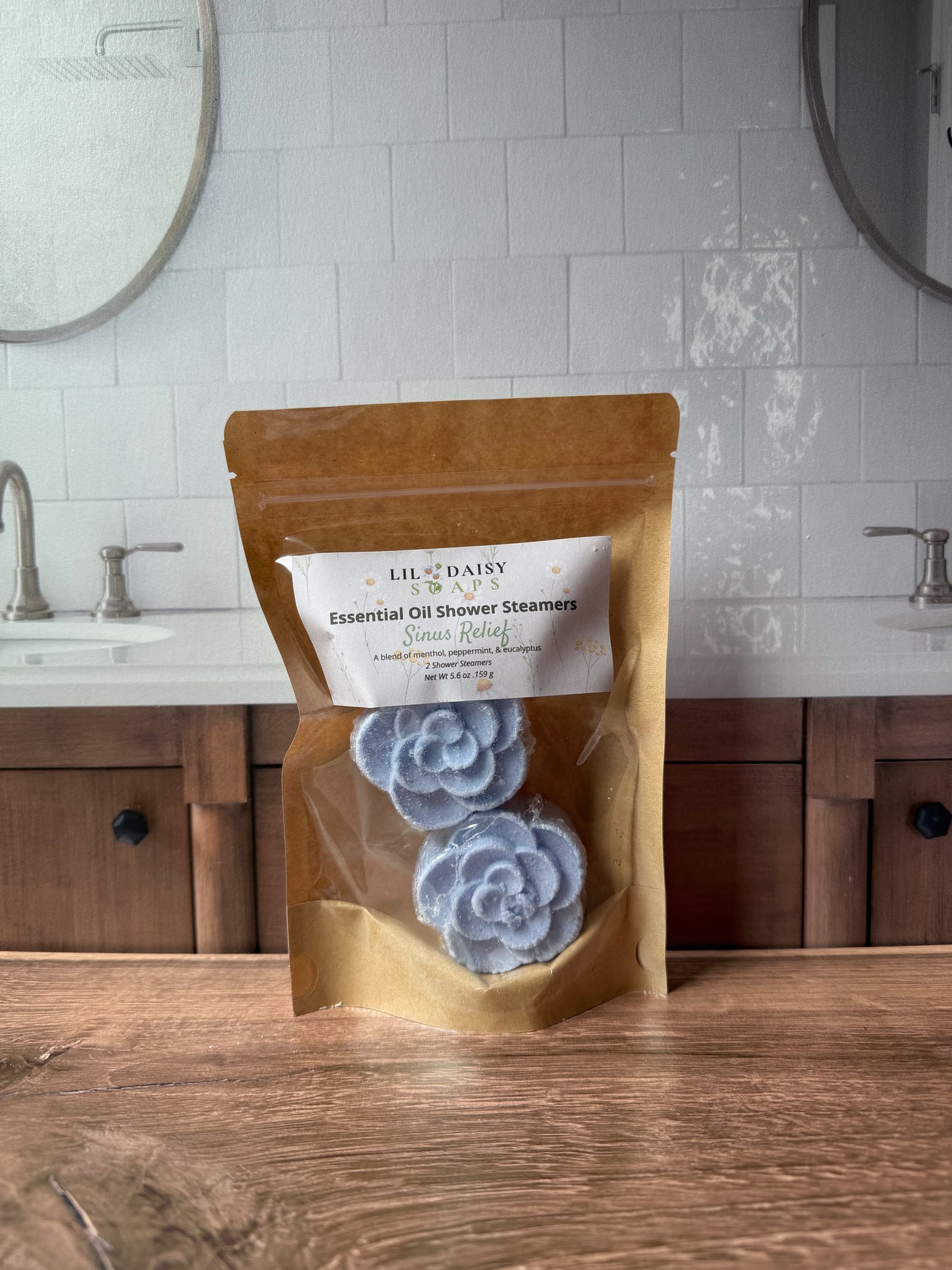A bag of Lil Daisy Soaps Essential Oil Shower Steamers rests on a wooden bathroom counter.
