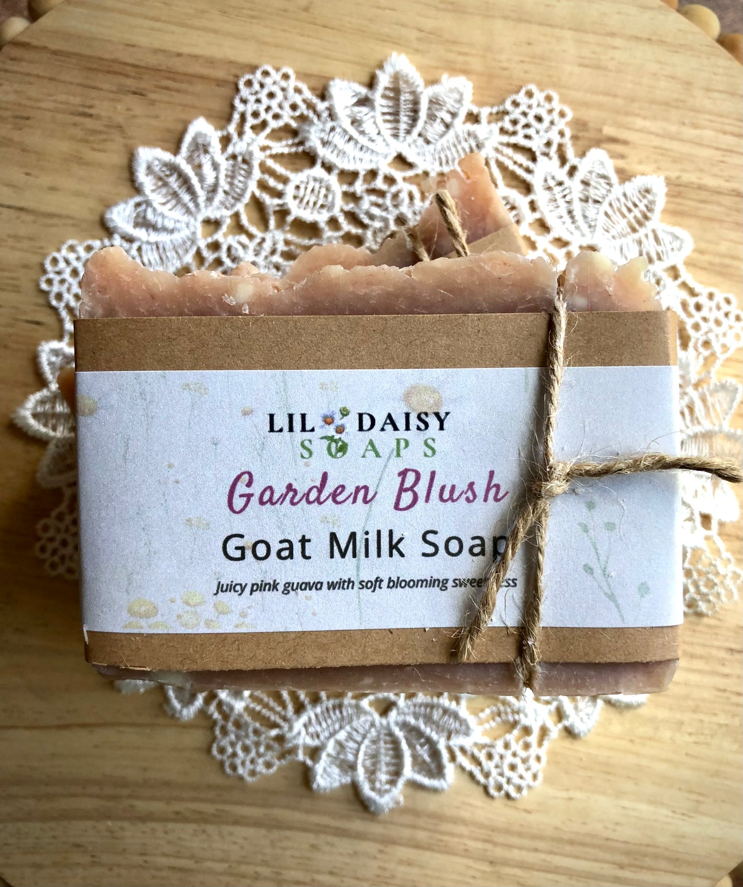 A Garden Blush Goat Milk Soap Bar by Lil Daisy Soaps sits on a lace doily, tied with twine.