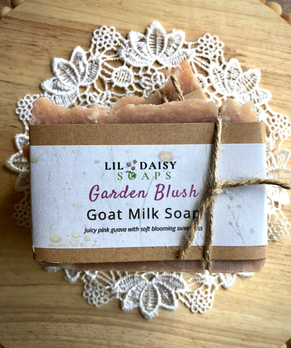 A Garden Blush Goat Milk Soap Bar by Lil Daisy Soaps sits on a lace doily, tied with twine.