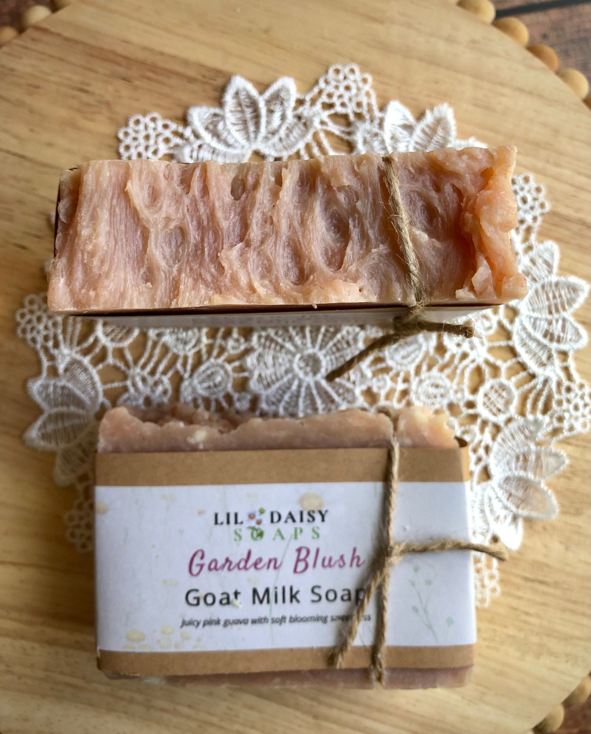 Two Garden Blush Goat Milk Soap Bars by Lil Daisy Soaps, one wrapped and one unwrapped, on a lace doily.