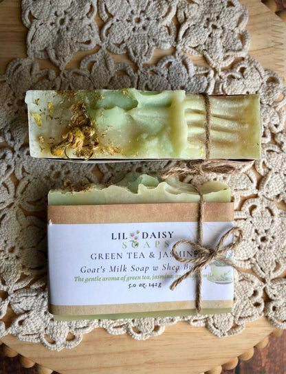 Two Lil Daisy Soaps Green Tea & Jasmine Goat Milk Soap bars, one tied with twine, sit on a lace doily.