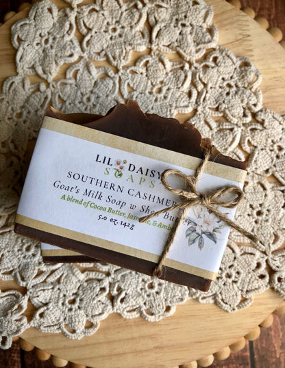 A bar of Lil Daisy Soaps Southern Cashmere Goat Milk Soap, wrapped in label and twine on a lace doily.