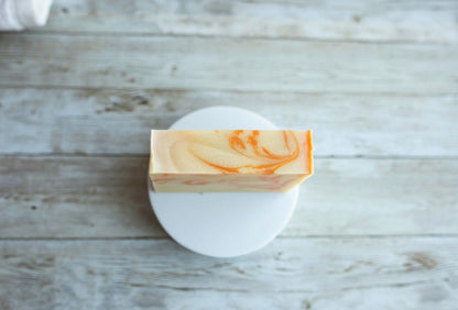 Lil Daisy Soaps’ Orange Patchouli Natural Goat Milk Soap Bar rests on a white dish atop a wooden surface.