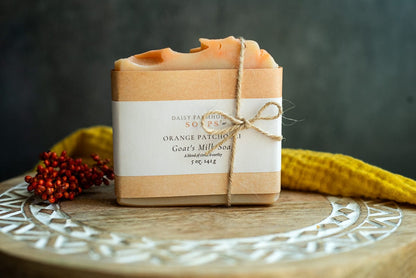 Lil Daisy Soaps Orange Patchouli Goat Milk Soap Bar, wrapped in paper and twine, on a wooden tray.