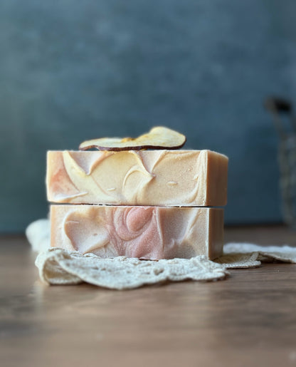 Two Lil Daisy Soaps Heirloom Apple Goat Milk Soaps, pink and cream swirled, stacked on lace on wood.