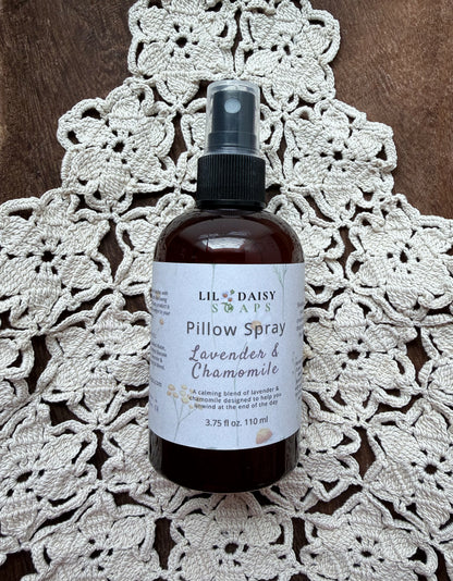 Lil Daisy Soaps’ Lavender & Chamomile Pillow Spray sits on a crocheted doily atop a wooden surface.