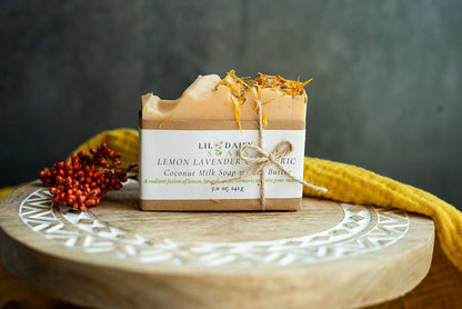A Lemon & Lavender Natural Goat Milk Soap Bar by Lil Daisy Soaps sits on a tray with flowers and a yellow cloth.