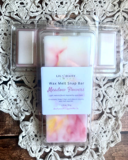 A Lil Daisy Soaps Meadow Flowers Wax Melt-Long Lasting Snap Bar in clear wrap on a doily and wood surface.