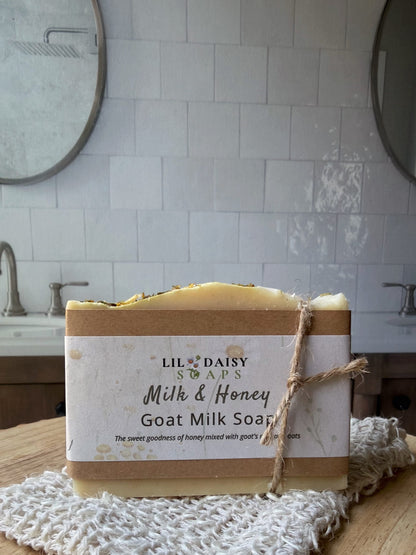 A Lil Daisy Soaps Milk & Honey Goat Milk Soap Bar with oats rests on a washcloth in a bathroom.