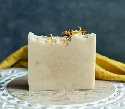 The Lil Daisy Soaps Milk & Honey Goat Milk Soap Bar with oats sits on a decorative wooden surface.
