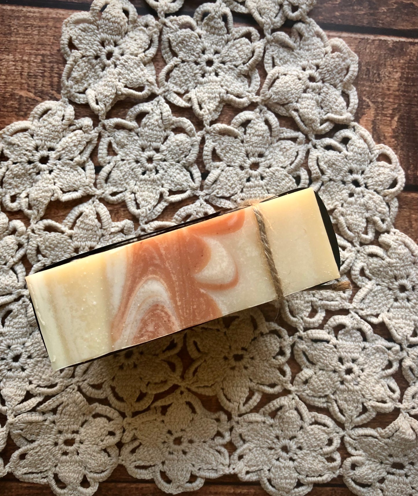 Lil Daisy Soaps’ Orange & Cedarwood Natural Goat Milk Soap with twine on a crochet doily atop wood.