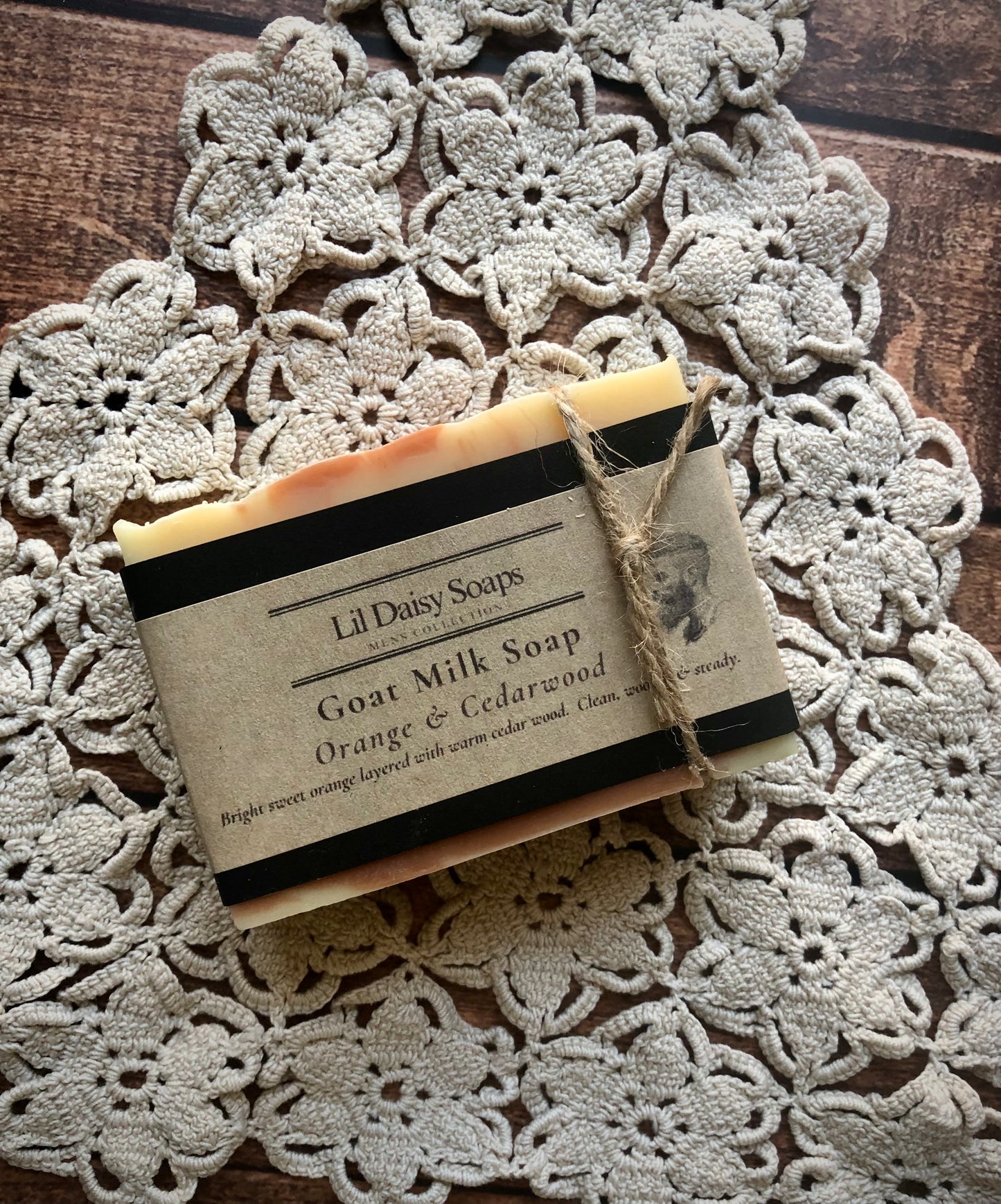 Lil Daisy Soaps Orange & Cedarwood Natural Goat Milk Soap bar on a crocheted doily, labeled rhassoul clay.