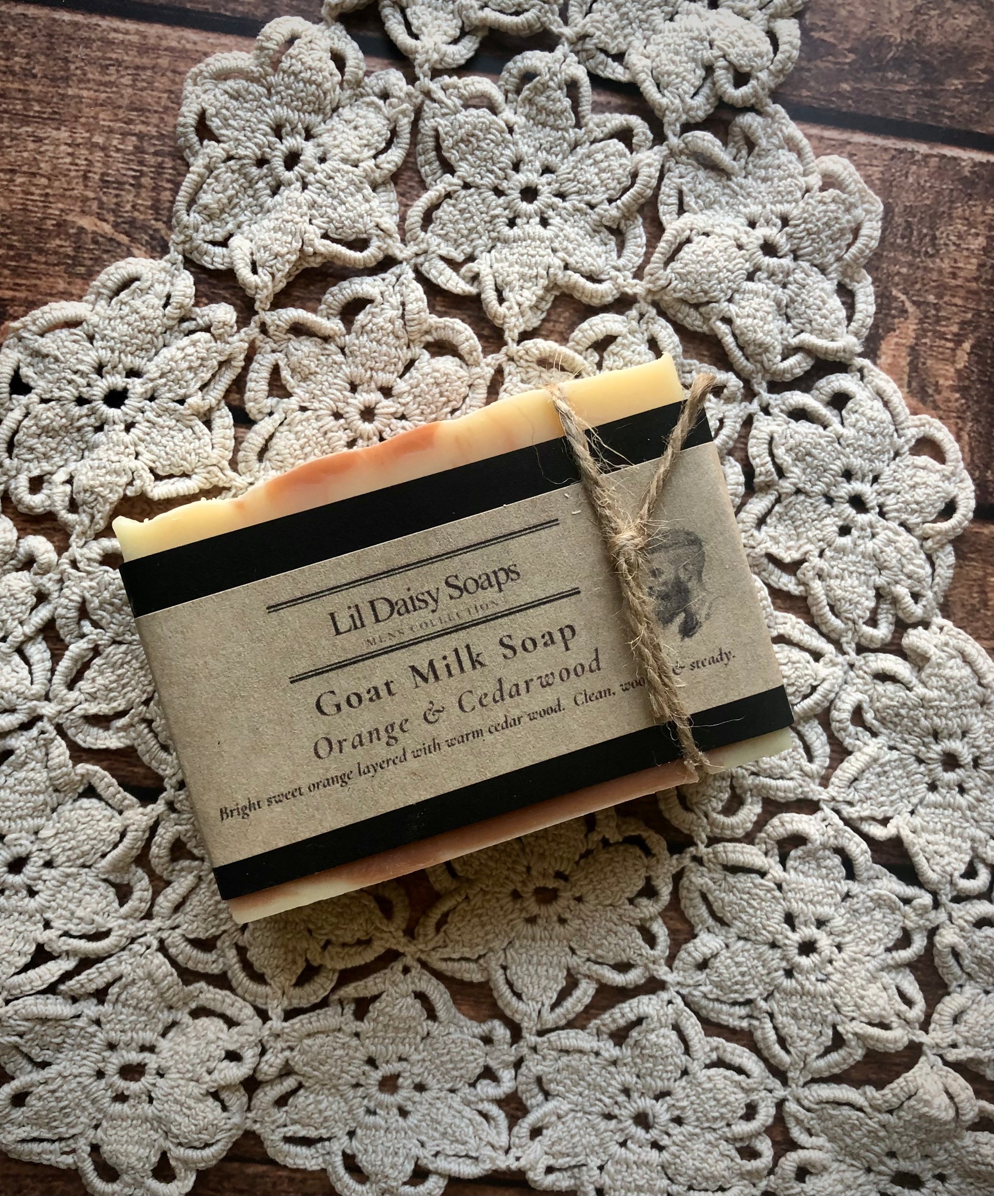 Lil Daisy Soaps Orange & Cedarwood Natural Goat Milk Soap bar on a crocheted doily, labeled rhassoul clay.