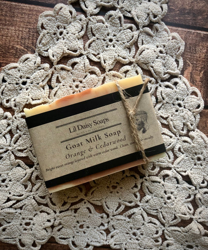 Lil Daisy Soaps Orange & Cedarwood Natural Goat Milk Soap bar on a crocheted doily, labeled rhassoul clay.