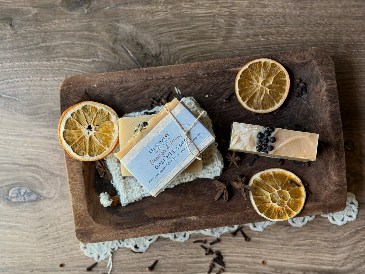 Lil Daisy Soaps’ Orange & Clove Goat Milk Soap bars with dried orange slices on a rustic wooden tray.