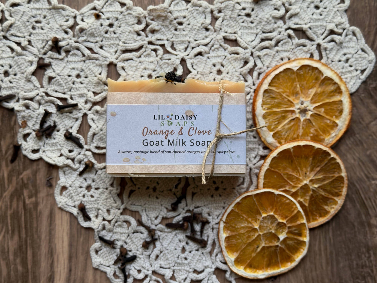 Lil Daisy Soaps Orange & Clove Goat Milk Soap rests on lace with dried oranges and cloves.
