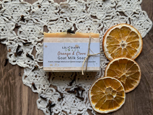 Lil Daisy Soaps Orange & Clove Goat Milk Soap rests on lace with dried oranges and cloves.