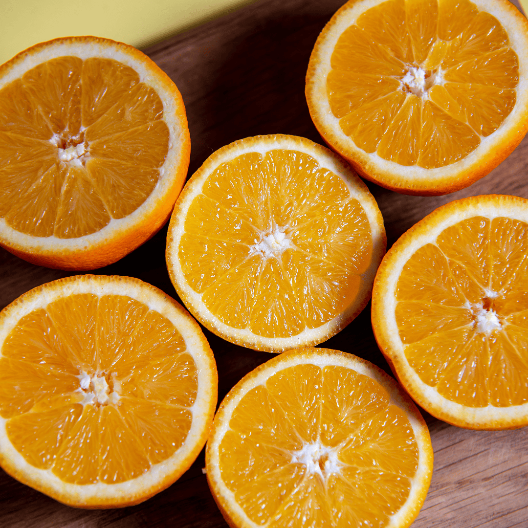 Six halved oranges next to Lil Daisy Soaps Orange Patchouli Natural Goat Milk Soap Bar on a wooden surface.