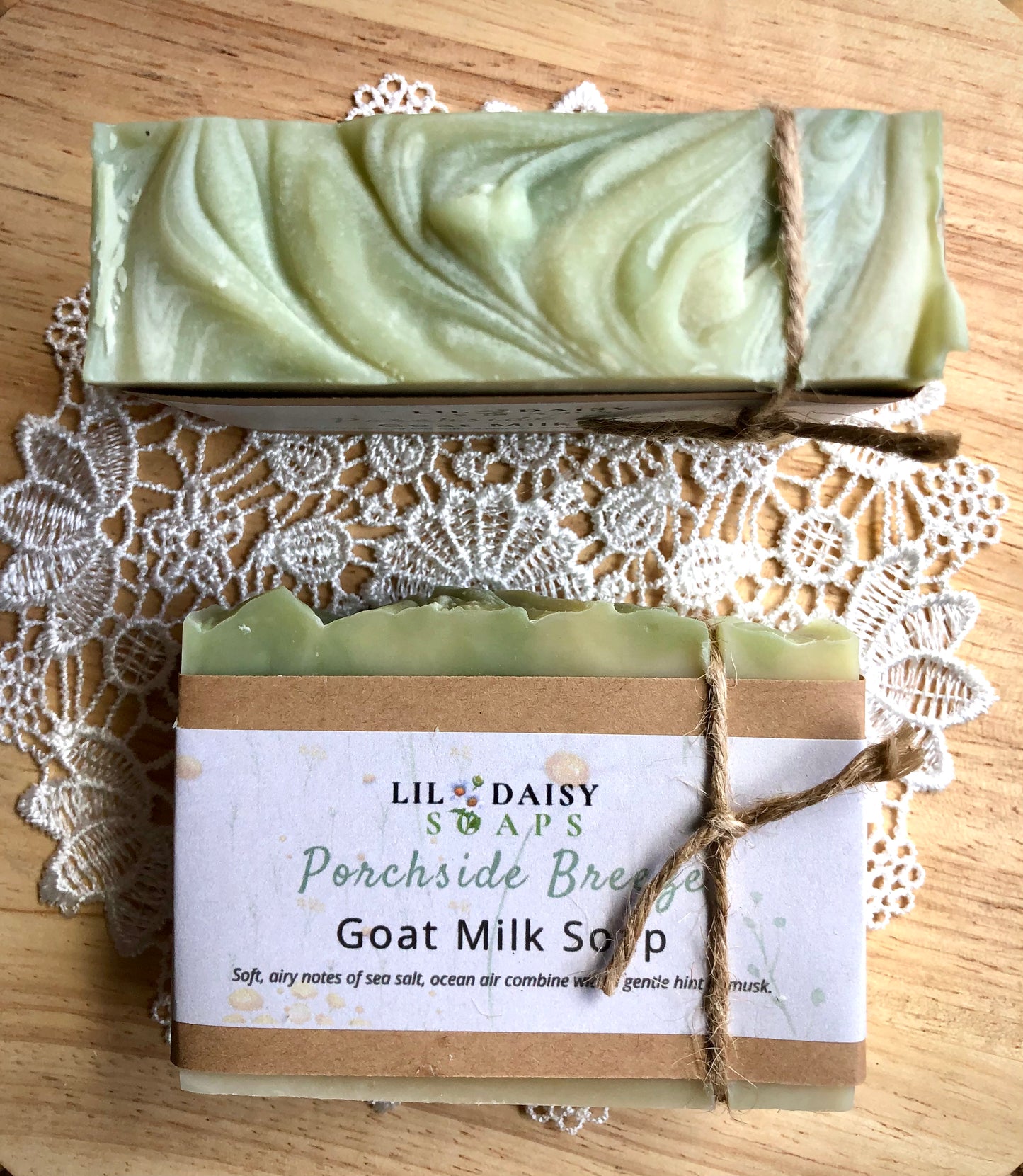 Two bars of Lil Daisy Soaps Porchside Breeze Goat Milk Soap on a doily atop a wooden surface.