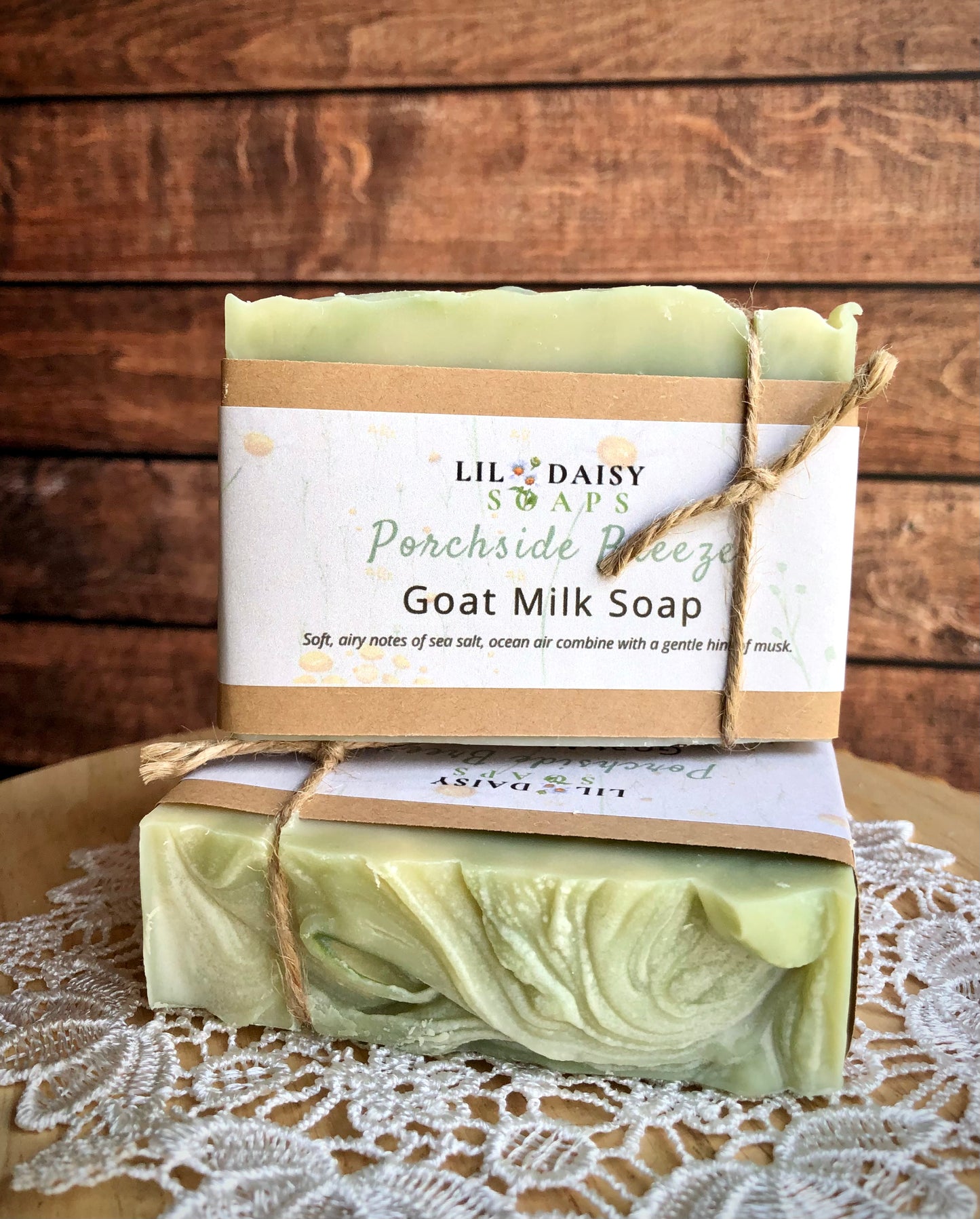 Two Porchside Breeze Goat Milk Soaps by Lil Daisy Soaps rest on lace with wood behind.