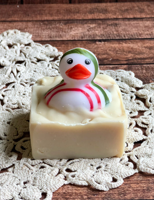 A rubber duck tops Lil Daisy Soaps’ Rubber Ducky Goat Milk Soap on a crocheted mat over wood.
