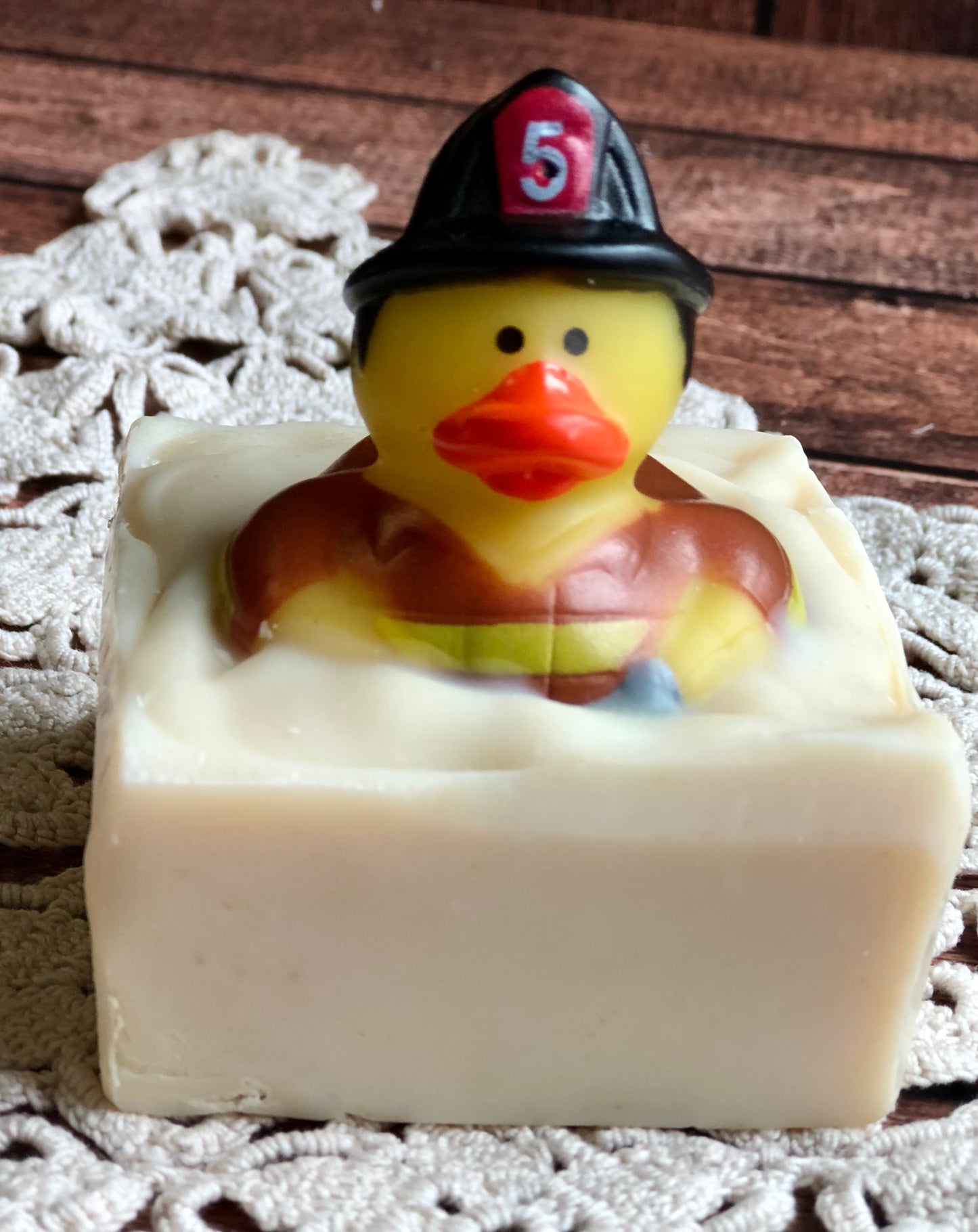 Lil Daisy Soaps Rubber Ducky Goat Milk Soap, firefighter-themed, sits on a crochet mat in a white bar.
