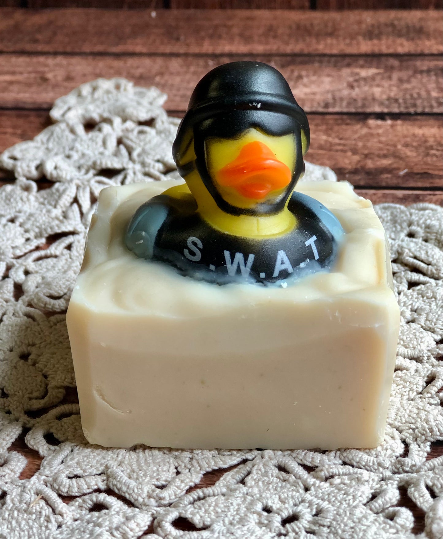 A SWAT duck tops Lil Daisy Soaps Rubber Ducky Goat Milk Soap on a lace doily and wooden surface.