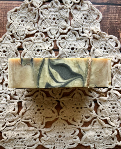 Lil Daisy Soaps Sandalwood & Musk Goat Milk & Beer Soap with twine sits on a floral doily on wood.