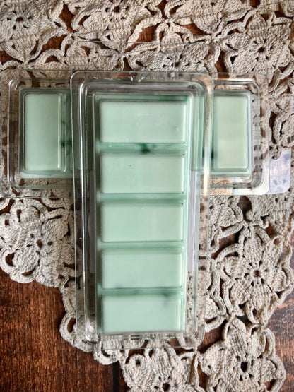 Three Snow Kissed Pines Snap Bar Wax Melts by Lil Daisy Soaps on a crocheted doily atop a wooden surface.