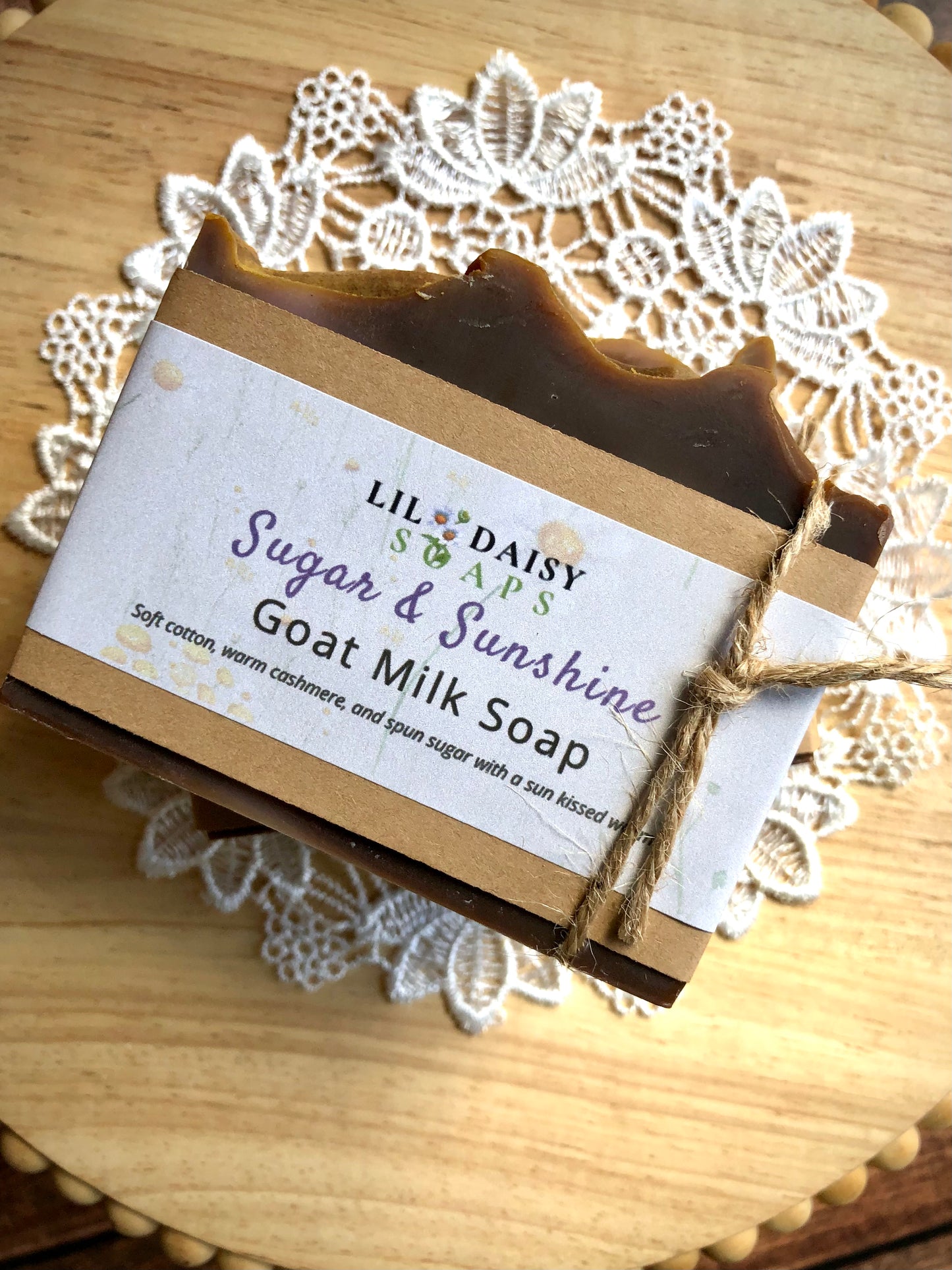 Sugar & Sunshine Goat Milk Soap by Lil Daisy Soaps, tied with twine on lace atop a wooden surface.