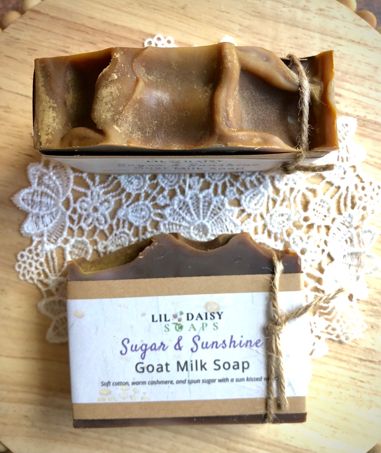 Two brown Lil Daisy Soaps Sugar & Sunshine Goat Milk Soap bars on a doily and wooden surface.