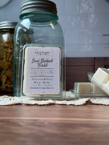 Sun Baked Field Soy Wax Melts by Lil Daisy Soaps sit on lace beside a blue jar and white tiles.