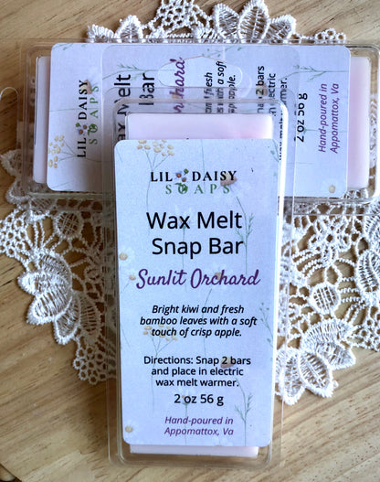 Two Lil Daisy Soaps Sunlit Orchard Wax Melt Snap Bars on a doily-covered wooden surface.