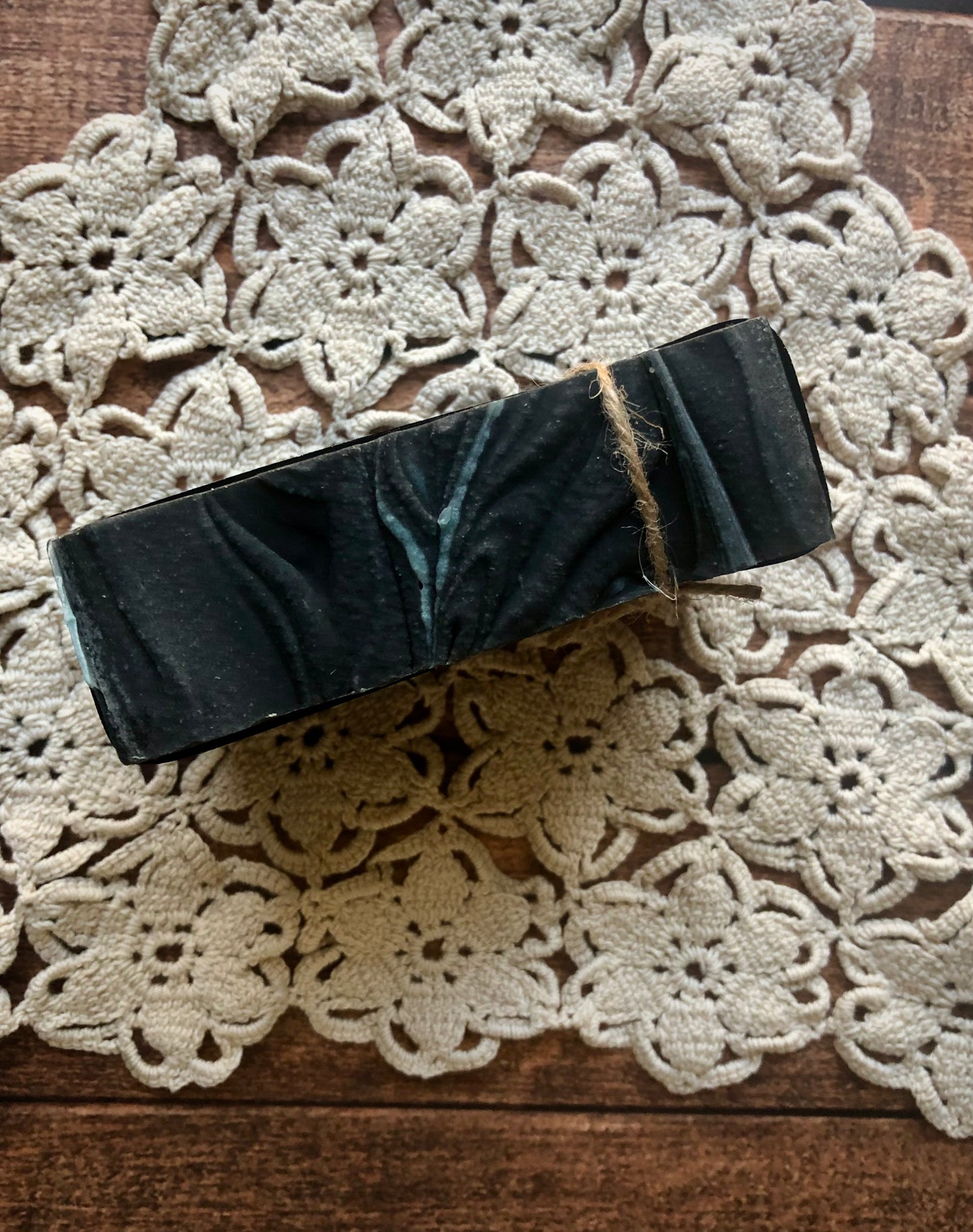 Lil Daisy Soaps’ Tobacco & Bayleaf Goat Milk Soap Bar, black marbled, boxed and twine-tied on a doily.
