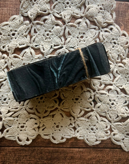Lil Daisy Soaps’ Tobacco & Bayleaf Goat Milk Soap Bar, black marbled, boxed and twine-tied on a doily.