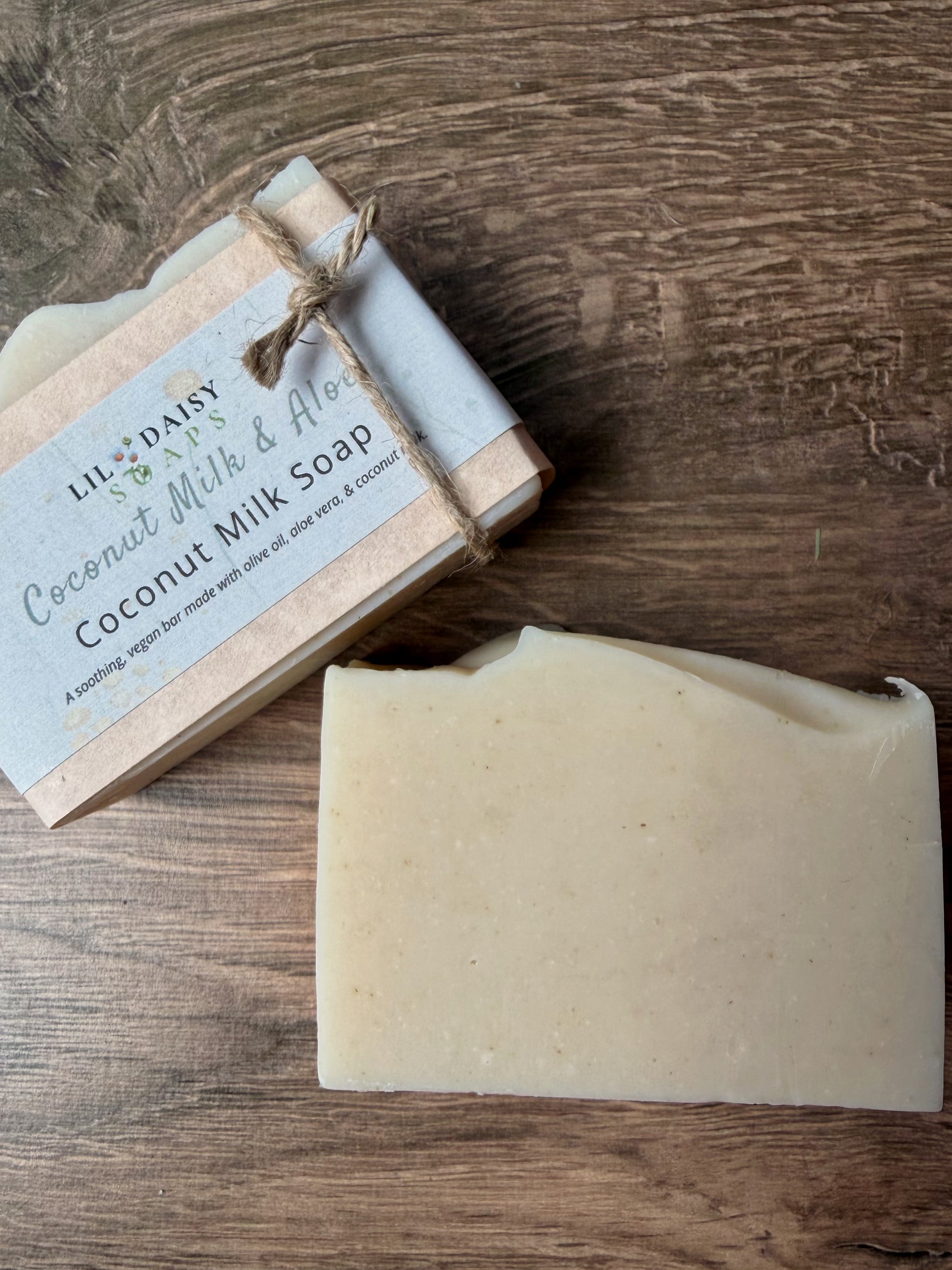 Two Lil Daisy Soaps Unscented Coconut Milk & Aloe bars, one wrapped in twine, rest on a wooden surface.